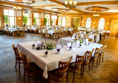 Elegante Hochzeitsfeier im Gasthof nahe München, festlich gedeckte Tische mit Dekoration und Stühlen im Saal.