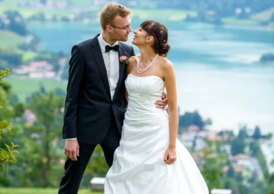 Brautpaar posiert vor malerischer Kulisse mit See bei Hochzeit auf Schliersberg-Alm. Hochzeitsfotografie in Oberbayern.