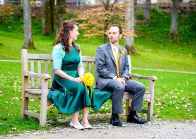 Brautpaar auf Bank im Kurpark Bad Toelz, Hochzeitsportrait mit Blumen und gruenem Hintergrund.