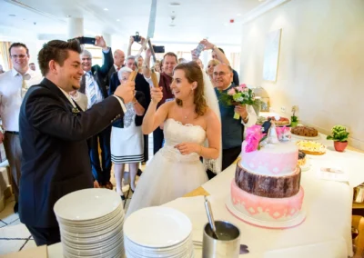 Hochzeitspaar schneidet Torte bei Feier in Oberbayern, umgeben von Gaesten und Fotografen. Hochzeitsfotografie.