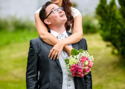 Brautpaarshooting im Garten von Schloss Sulzemoos. Braut mit Blumenstrauss umarmt lachenden Bräutigam.