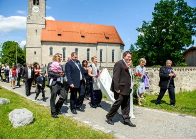 Hochzeitsgesellschaft bei kirchlicher Trauung vor Kirche in Oberbayern, festlich gekleidete Gaeste und Brautpaar.