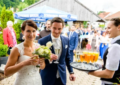 Brautpaar mit Sektgläsern und Blumenstrauß, Empfang bei Hochzeit im Eventstadl zur Alten Säge, Hochzeitsfotografie.