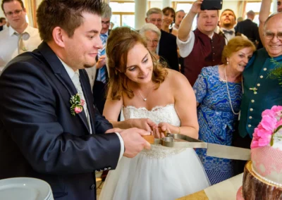 Brautpaar schneidet Hochzeitstorte in Grosshartpenning, umgeben von Gaesten. Hochzeitsfotografie in Oberbayern.