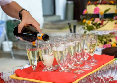 Person schenkt Champagner bei Hochzeit am Schliersberg-Alm ein. Hochzeitstorte mit Blumen im Hintergrund.