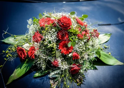 Roter Blumenstrauss auf Autodach bei Hochzeit in Oberbayern. Hochzeitsfoto von Hochzeitsfotograf in Tegernsee.