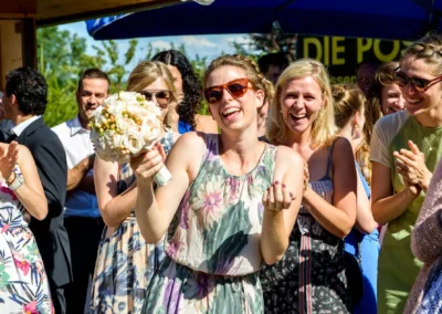 Brautstrausswerferin laechelnd bei Hochzeitsreportage in Gasthof zur Post. Freude und Applaus bei sonnigem Hochzeitstag.