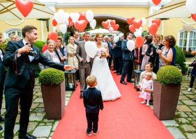 Brautpaar und Gäste mit Luftballons auf rotem Teppich bei Hochzeit im Gutsgasthof Stangl, festgehalten von Hochzeitsfotograf.