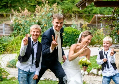 Brautpaar mit Kindern bei Hochzeitsreportage in Glonn, lachend im Garten. Hochzeitsfoto von Hochzeitsfotografen.