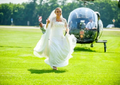 Braut in weissem Kleid laeuft auf Wiese bei Hochzeit in Neukeferloh, im Hintergrund ein Hubschrauber. Hochzeitsfoto.