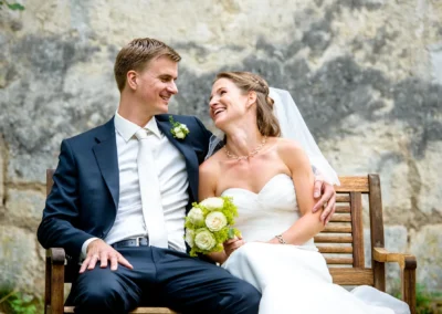 Brautpaar lacht auf einer Bank in Gut Georgenberg, Hochzeitsfotograf aus München. Hochzeitsportrait in Oberbayern.