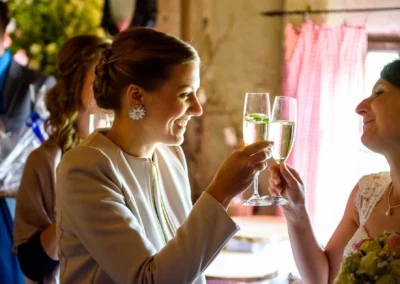 Zwei Frauen stoßen mit Sekt bei einer Hochzeit in Moosach bei Grafing an. Hochzeitsfoto zeigt freudige Stimmung.