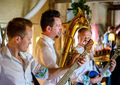 Musiker spielen auf Hochzeit in Moosach bei Grafing. Saxophon und Gitarren im Eventstadl zur Alten Saege. Hochzeitsfoto.