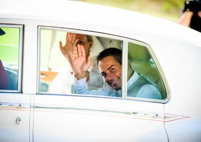 Braut und Bräutigam winken aus einem Auto bei einer Hochzeit in der Alten Gaertnerei Taufkirchen.
