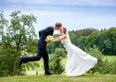 Brautpaar beim Lachen auf einer Wiese in Gut Georgenberg, Brautstrauss in Hand. Hochzeitsfotografie im Freien.