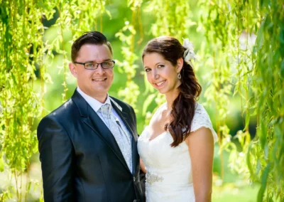 Brautpaarshooting im Gruenen bei Gut Schloss Sulzemoos. Hochzeitsportrait mit Braut in weissem Kleid und Bräutigam im Anzug.