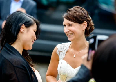 Braut bei ihrer Hochzeit im Gespraech mit Gast, lachend, in Moosach bei Grafing. Hochzeitsfotografie in Oberbayern.