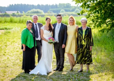Brautpaar mit Familie bei Hochzeit im Freien auf Gut Schloss Sulzemoos, strahlender Sonnenschein und grüne Wiese.