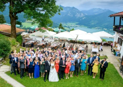 Hochzeitsgesellschaft bei einer Feier in Schliersberg-Alm, mit Blick auf See und Berge. Hochzeitsreportage in Oberbayern.