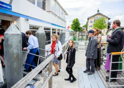 Gäste betreten ein Boot bei einer Hochzeitsreise am Tegernsee, festgehalten von einem Hochzeitsfotografen.