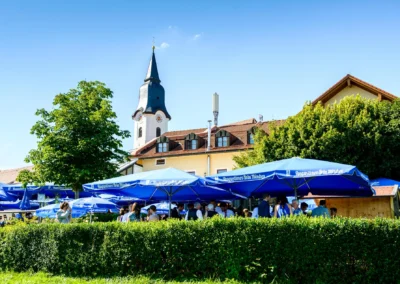Gartenempfang bei einer Hochzeit nahe Starnberger See mit blauen Schirmen und Kirchturm im Hintergrund.