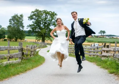 Brautpaar springt glücklich auf Landstraße bei Gut Georgenberg, festgehalten von einem Hochzeitsfotografen aus Oberbayern.