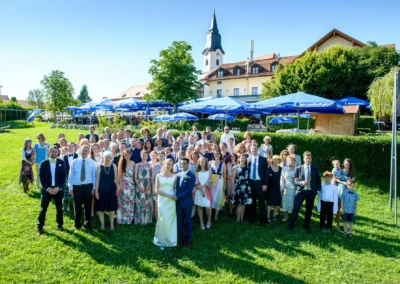 Hochzeitsfoto in Aufkirchen, Gruppe von Gaesten im Freien vor Gasthof zur Post, blauer Himmel im Hintergrund.