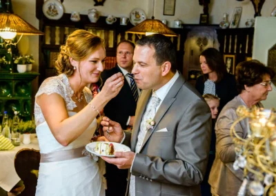 Braut fuettert Bräutigam mit Kuchen bei Hochzeit im Gasthof Stangl, Neufarn bei München. Hochzeitsfotografie.