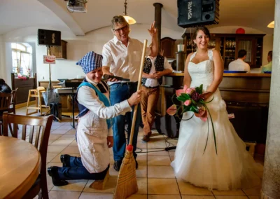 Braut lacht bei Hochzeitsfeier in Gasthof Widmann nahe Muenchen, begleitet von feiernden Gaesten. Hochzeitsreportage.