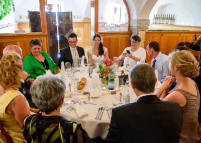 Gaste sitzen um einen festlich gedeckten Tisch bei einer Hochzeit auf Schloss Sulzemoos. Hochzeitsreportage.