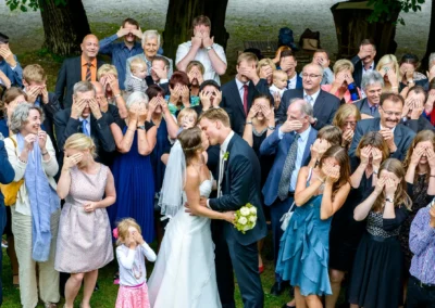 Brautpaar küsst sich vor Hochzeitsgästen mit verdeckten Augen. Hochzeitsfotografie auf Gut Georgenberg.