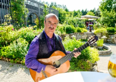 Ein Musiker spielt Gitarre bei einer Hochzeit in der Alten Gaertnerei Taufkirchen, umgeben von Gruen und Blumen.