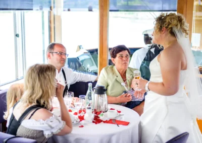 Braut im Gespraech mit Gaesten bei Hochzeit in Tegernsee, Hochzeitsfotografie zeigt entspannte Atmosphaere am Tisch.