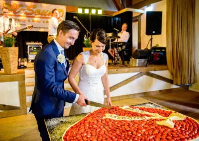 Brautpaar schneidet Hochzeitstorte bei Feier in Moosach bei Grafing, musikalisch begleitet von Band im Hintergrund.