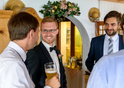Gruppen von Maennern in Anzuegen bei einer Hochzeitsfeier in Schliersberg-Alm, lachen und unterhalten sich. Hochzeitsfoto.