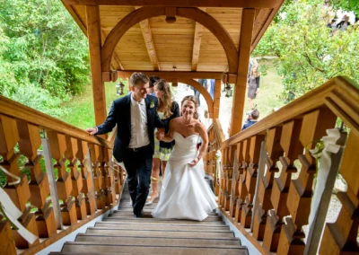 Brautpaar steigt lachend eine mit Holz verzierte Treppe hinauf. Hochzeitsfoto in Glonn, Oberbayern.