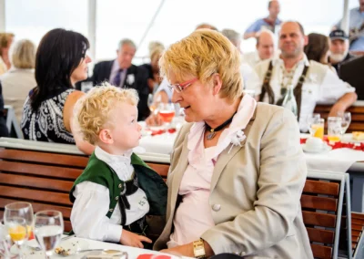 Kleines Kind in Tracht im Gespräch mit Frau bei Hochzeitsfeier in Oberbayern. Hochzeitsfoto in geselliger Runde.