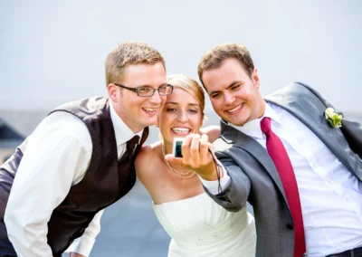 Braut lächelt mit zwei Gästen bei Hochzeitsreportage in Fürstenfeldbruck, perfekte Hochzeitsfotografie im Freien.