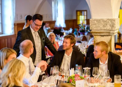 Gäste bei einer Hochzeitsfeier auf Gut Schloss Sulzemoos diskutieren am Tisch in eleganter Atmosphäre.