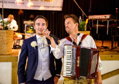 Bräutigam und Akkordeonspieler bei Hochzeit in Moosach bei Grafing, Hochzeitsfotografie mit lebendiger Musik.