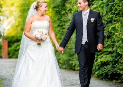 Brautpaar bei Hochzeitsportrait in Taufkirchen bei Muenchen, spazierend auf Allee, festgehalten in Hochzeitsfotografie.