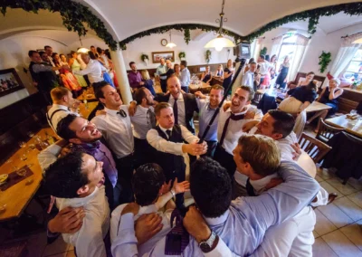 Hochzeitsgesellschaft feiert im Gasthof Widmann; Maenner in Anzug umarmen sich fröhlich bei Hochzeit in Gilching.