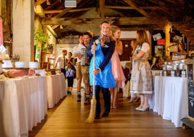 Hochzeitsreportage im Eventstadl zur Alten Säge: Gäste in Tracht, einige musizieren, ein Mann fegt den Boden.