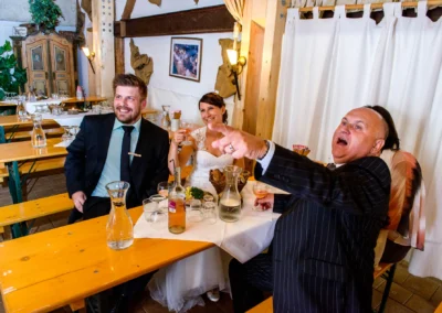 Hochzeitsreportage bei der Hochzeit in Moosach bei Grafing, Brautpaar und Gaeste lachen an Tisch.