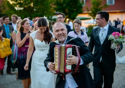 Hochzeit auf Gut Schloss Sulzemoos: Braut und Akkordeonspieler in festlicher Stimmung, Hochzeitsreportage.