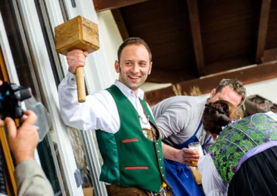 Mann in Tracht hebt Holzhammer bei Hochzeit, Moarwirt Hechenberg. Hochzeitsreportage, festlicher Moment.