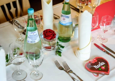 Hochzeitsfoto in Kreuth: Gedeckter Tisch mit Glaesern, roten Rosen und Lebkuchenherz bei einer Hochzeit.