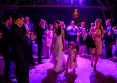 Braut in weissem Kleid tanzt mit Kind bei Hochzeit bei Gut Schloss Sulzemoos, umgeben von applaudierenden Gaesten.
