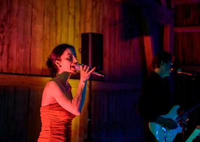 Sängerin und Gitarrist performen bei Hochzeit im Gut Schloss Sulzemoos, farbige Lichter erhellen die Szene. Hochzeitsfotograf.