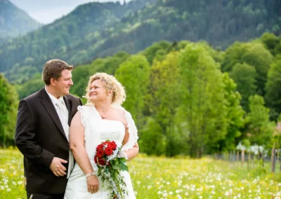 Brautpaar posiert auf blumenreicher Wiese mit Bergen im Hintergrund, Bayern. Hochzeitsfoto von einem Fotografen aus Kreuth.